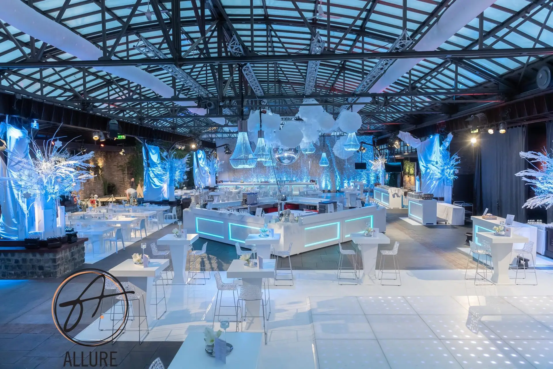 Evenementenhal in winterthema met witte statafels, verlichte bars en kristallen kroonluchters
